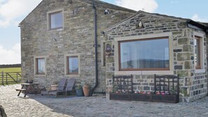 A stone building with a large window, a small attached structure with a bell, and a paved area with chairs and tables. - Ground Floor: 
Open plan living space. (Silsden near Skipton)