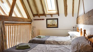 A bedroom with two beds, wooden beams, a window, a radiator, and a painting on the wall. - 4 bedroom accommodation in Compton, near Chichester (Compton, near Chichester)
