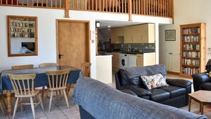 A cozy living room with a dining area, a kitchen, and a loft bedroom with a wooden balcony. - 4 bedroom accommodation in Compton, near Chichester (Compton, near Chichester)