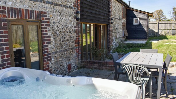 A hot tub in a backyard with a brick wall, wooden deck, and a table with chairs. - 4 bedroom accommodation in Compton, near Chichester (Compton, near Chichester)