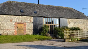A stone building with a sloped roof, a wooden door, and a large window. - 4 bedroom accommodation in Compton, near Chichester (Compton, near Chichester)