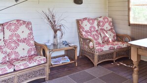 A room with two wicker chairs with floral upholstery, a small table with a vase and decorative items, and a wooden beam overhead.