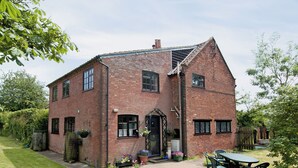 Een tweelaags bakstenen huis met een veranda, een kleine tuin en een terras met tuinmeubilair.
