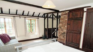 Een slaapkamer met een groot bed, een raam met gordijnen, een houten trap en een bakstenen muur.