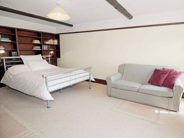 Une chambre à coucher avec un lit, une table de chevet, une lampe, une bibliothèque et un fauteuil à rayures.