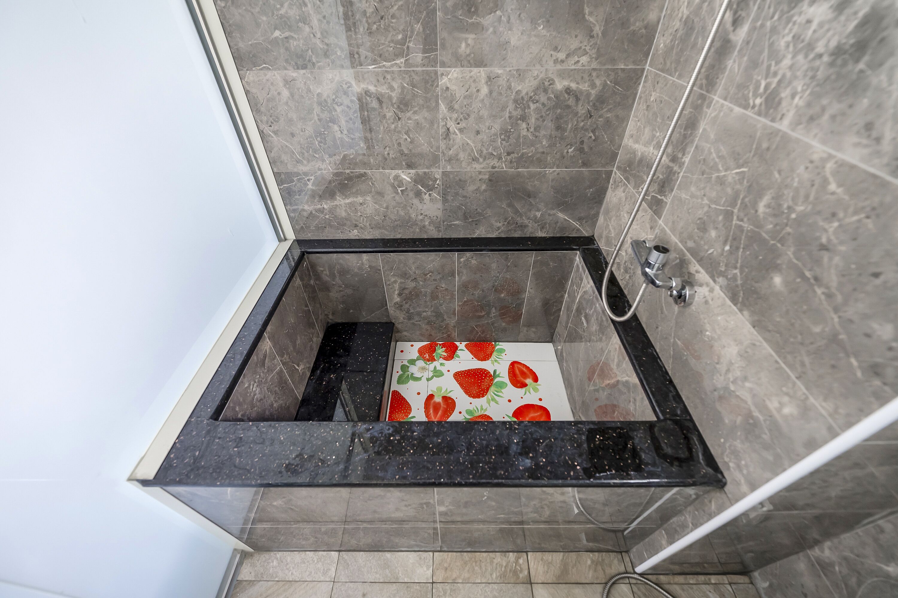 A shower with a black marble tub and a tiled floor.