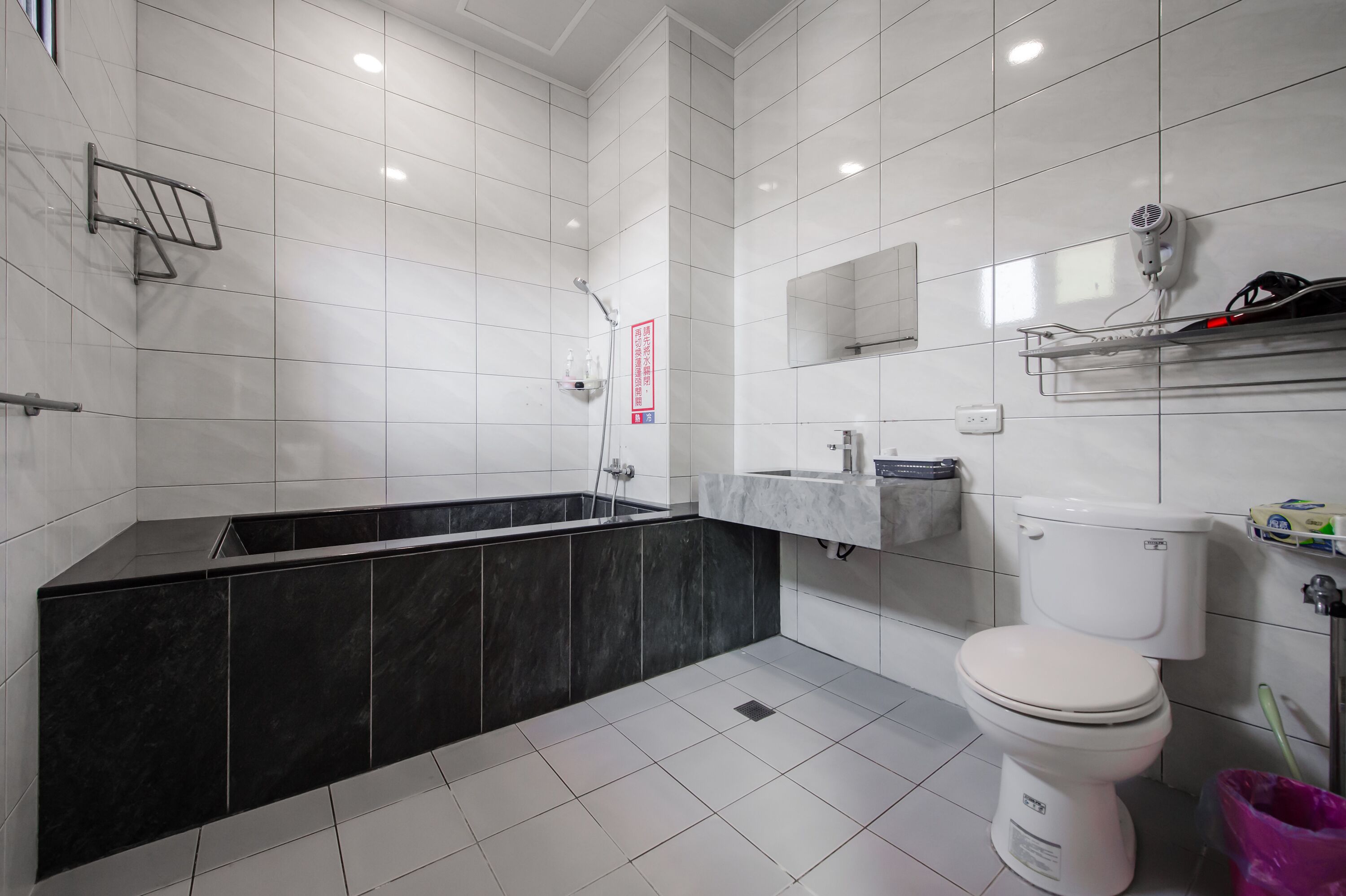 A modern bathroom with a black bathtub, white toilet, and a shower area.