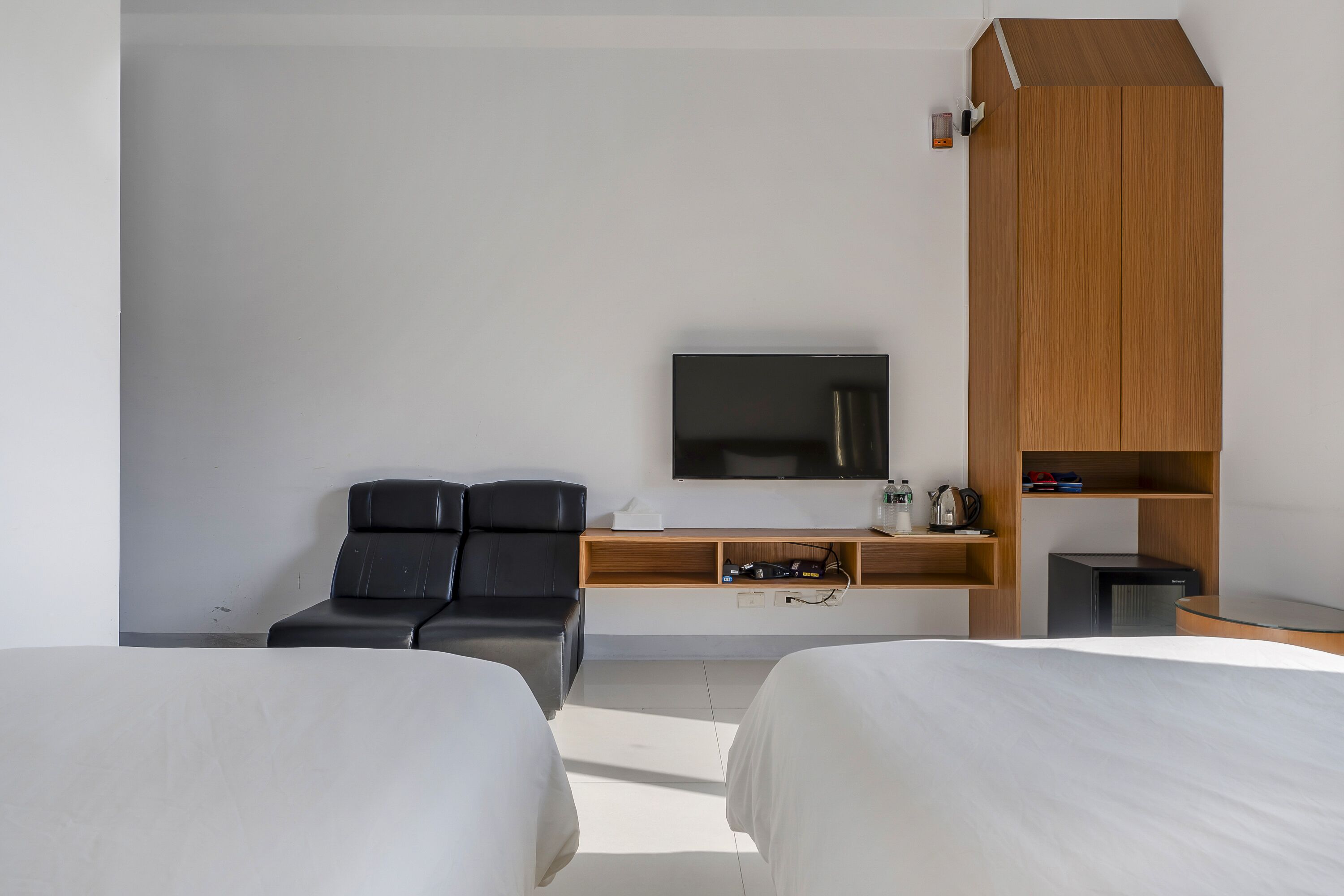 A modern hotel room with two beds, a TV, a wooden cabinet, a desk, and a black leather chair.