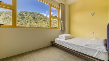 Un dormitorio con cama, ventana que ofrece vistas a una colina boscosa y pared amarilla.