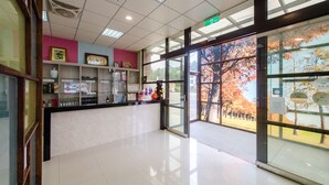 A reception area with a glass door leading outside, a reception desk, and a wall with shelves displaying various items. - Quan Ming Line Museum (Dahu)