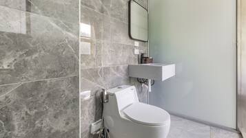 A modern bathroom with a white toilet, a marble-tiled wall, a glass shower enclosure, and a white sink.