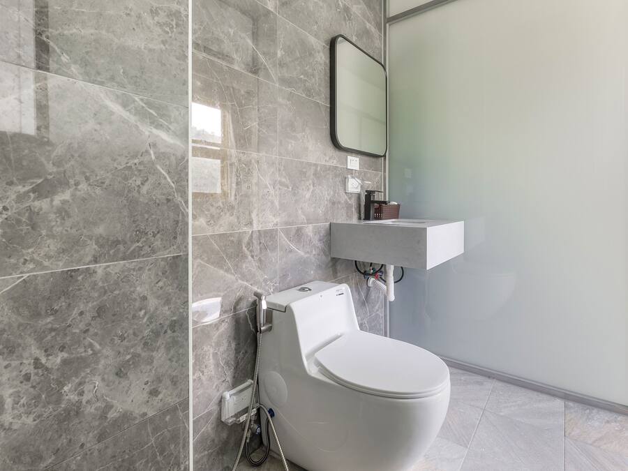 A modern bathroom with a white toilet, a marble-tiled wall, a glass shower enclosure, and a white sink.