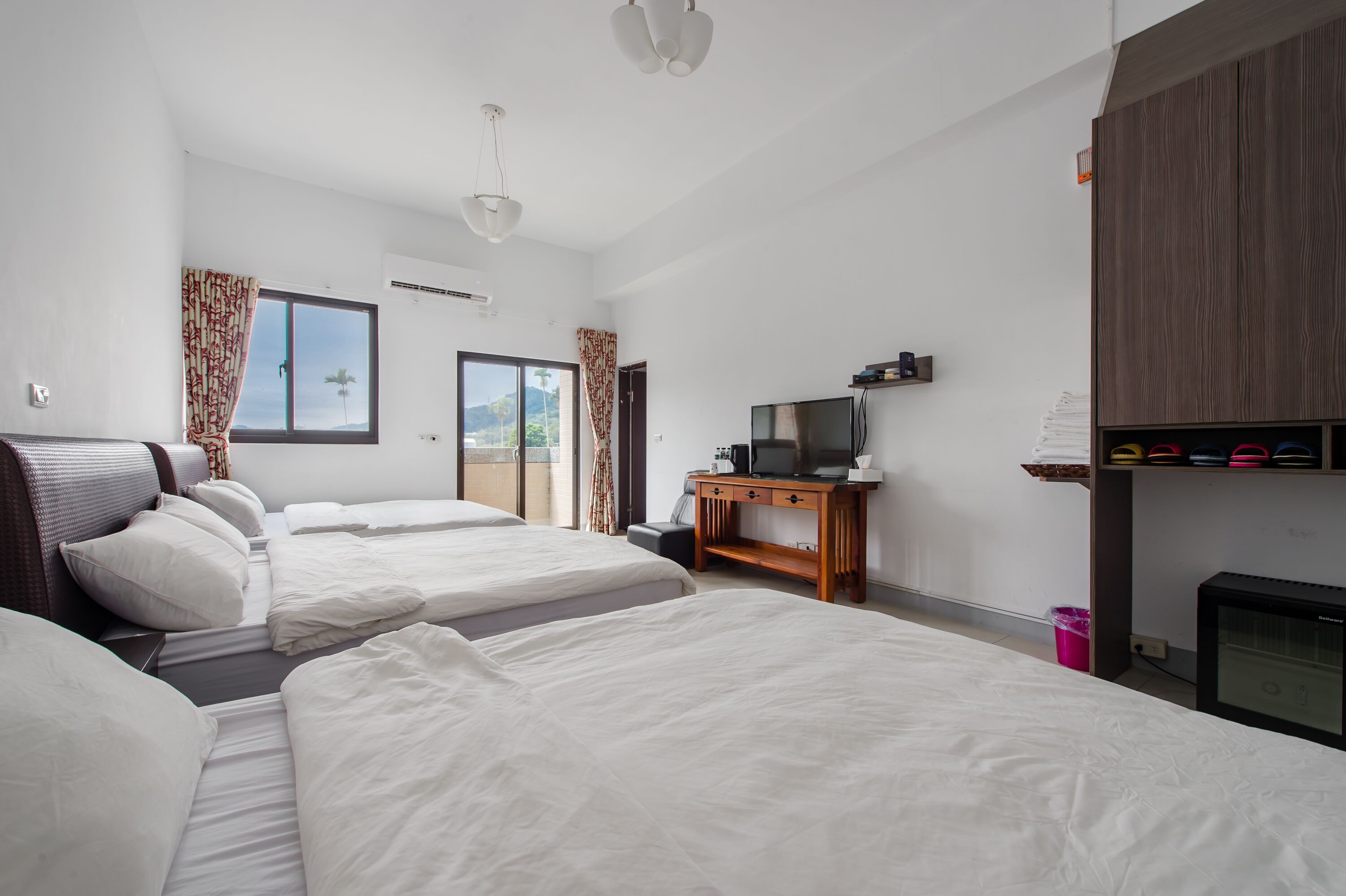 A hotel room with two beds, a television, a desk, and a window with curtains.