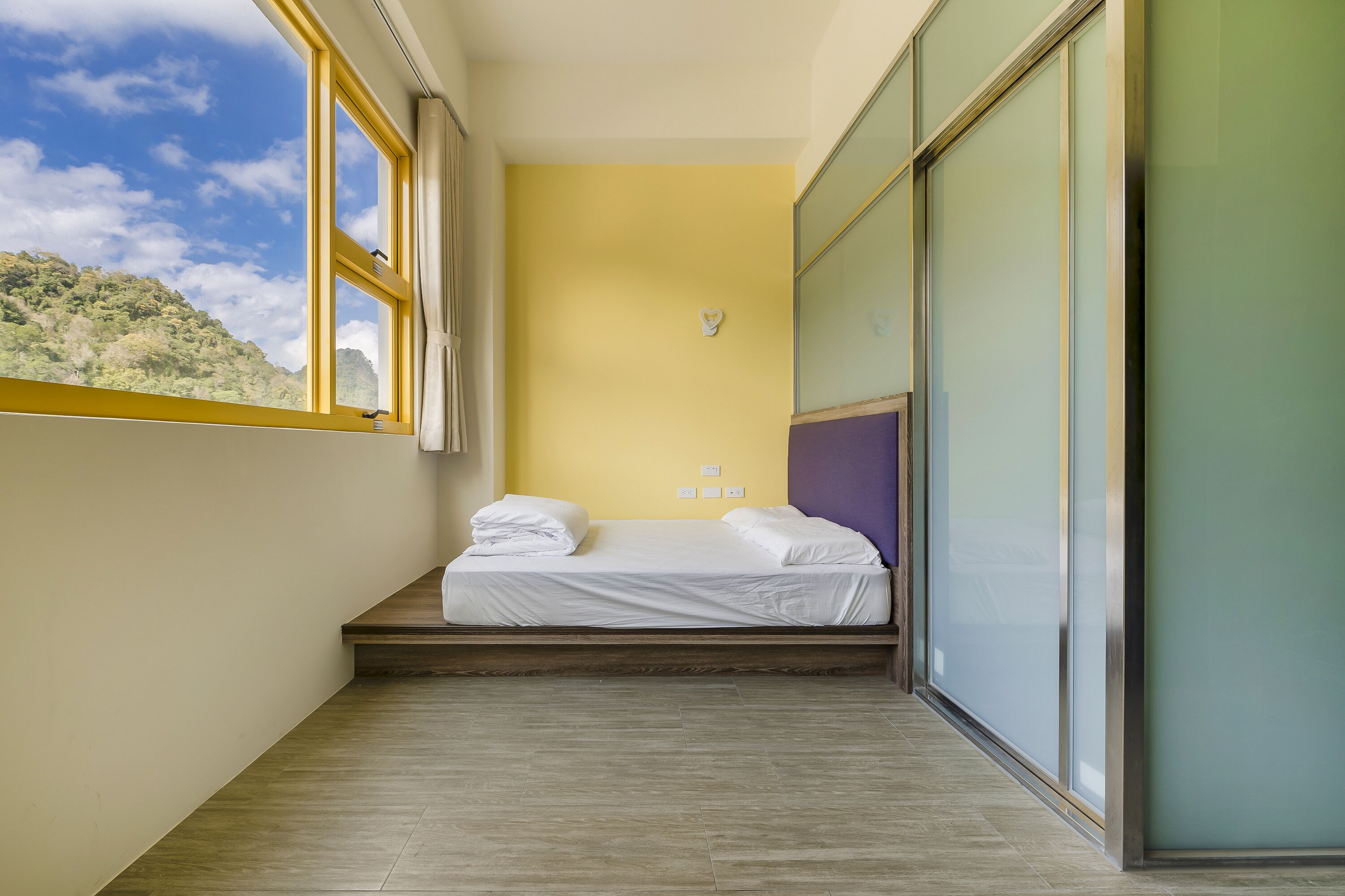 A small, narrow room with a bed, a window, and a view of a mountain.