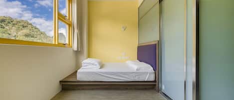 A small, narrow room with a bed, a window, and a view of a mountain.