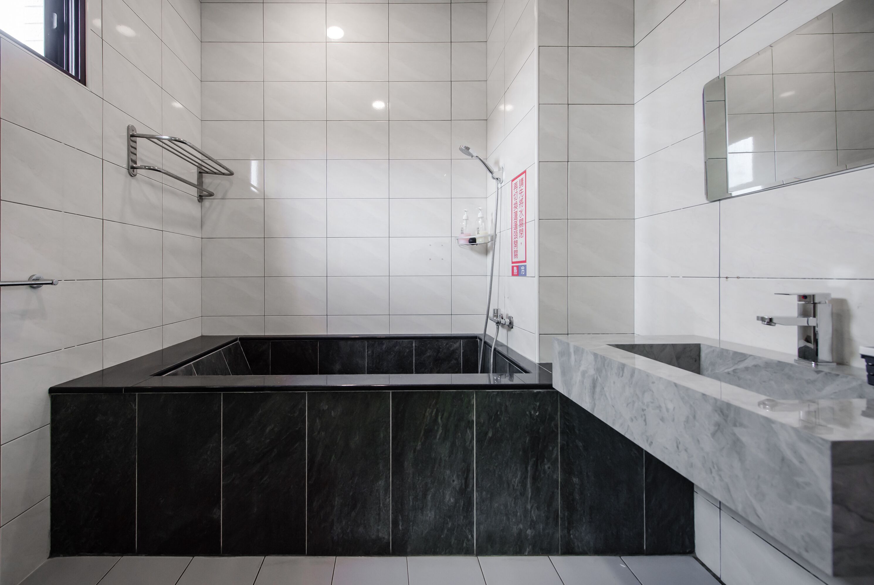 A modern bathroom with a black bathtub, a marble vanity, and a large mirror.
