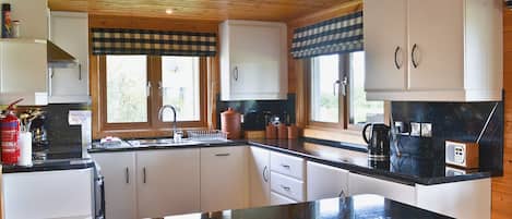 A kitchen with wooden cabinets, a black countertop, and a window with a checkered valance.