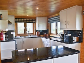 A kitchen with wooden cabinets, a black countertop, and a window with a checkered valance.