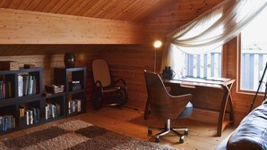 Un accogliente interno di una baita con soffitto in legno, una scrivania con una sedia, una libreria e una finestra con tende.