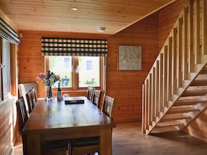 A wooden interior with a dining table, chairs, a vase with flowers, a map on the wall, and a wooden staircase.