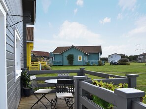 A patio with a table and chairs, a yellow fence, and a blue house in the background.