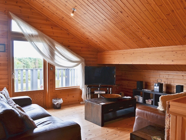 A cozy cabin interior with a wooden ceiling, a television, a wooden table, and a couch.