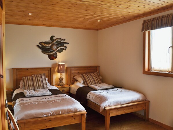 A room with two wooden beds, a wall-mounted lamp, and a window with curtains. - 2 bedroom accommodation in Fritton, near Great Yarmouth (Fritton, near Great Yarmouth)