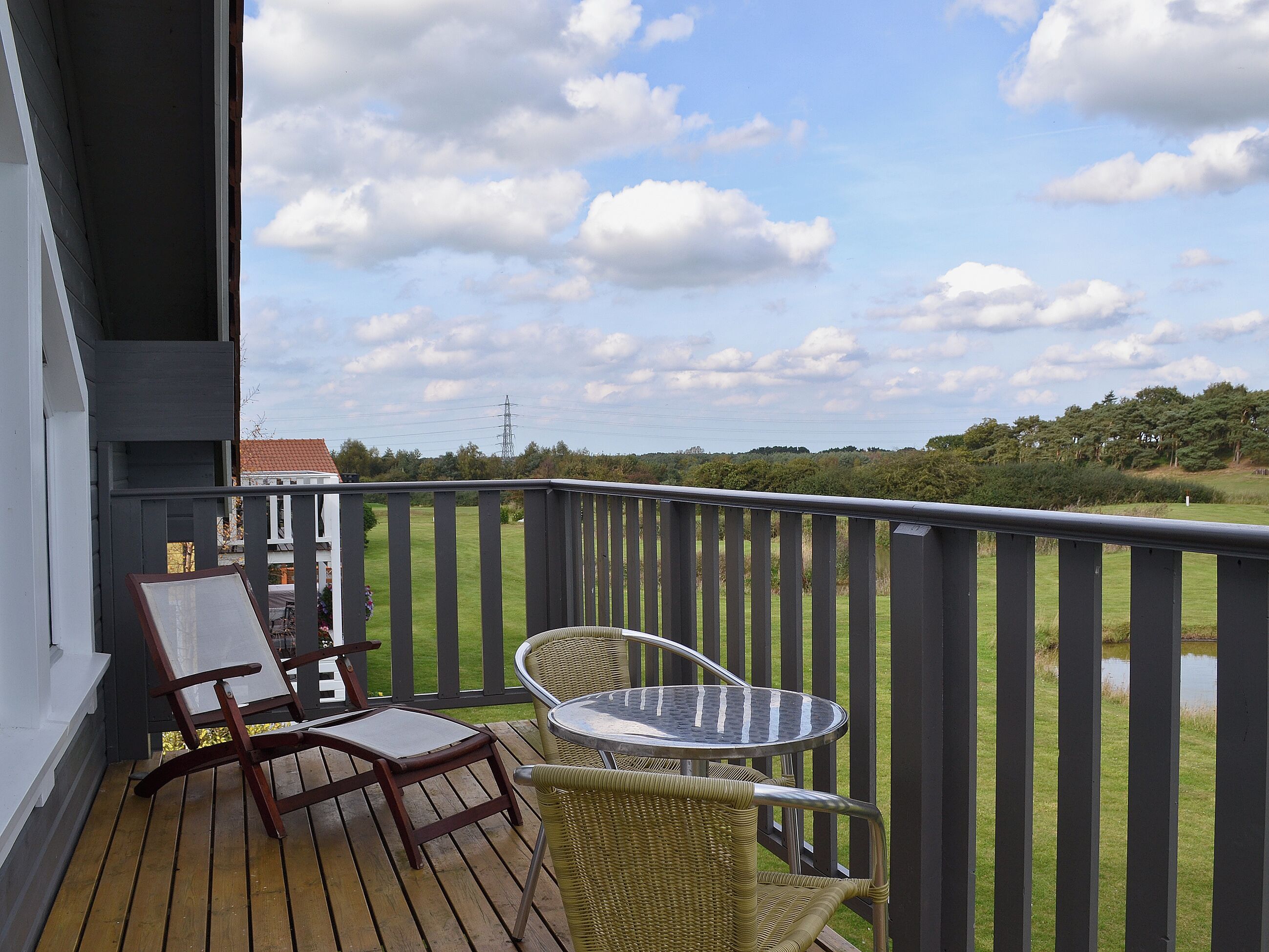 Un balcon doté d’une terrasse en bois, de deux fauteuils en osier et d’une petite table ronde.