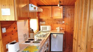 A compact kitchen with wooden cabinets, a microwave, a small refrigerator, and a stove. - 1 bedroom accommodation in Keswick (Keswick)