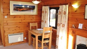 A wooden cabin interior with a dining table, chairs, a framed picture, a radiator, and a fireplace. - 1 bedroom accommodation in Keswick (Keswick)