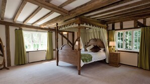 Een traditioneel hemelbed met houten hoofdeinde, geplaatst onder een schuine balkenplafond.