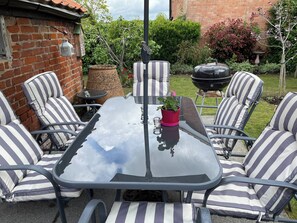 A patio with a glass table surrounded by striped chairs, a potted plant, and a barbecue grill. - 2 bedroom accommodation in Sproughton (Sproughton)