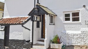 Un bâtiment blanc avec un toit recouvert de tuiles, une porte noire et une petite fenêtre.