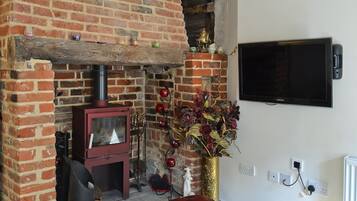 Un salon chaleureux avec une cheminée en briques, un pouf en cuir rouge et un téléviseur à écran plat fixé au mur.