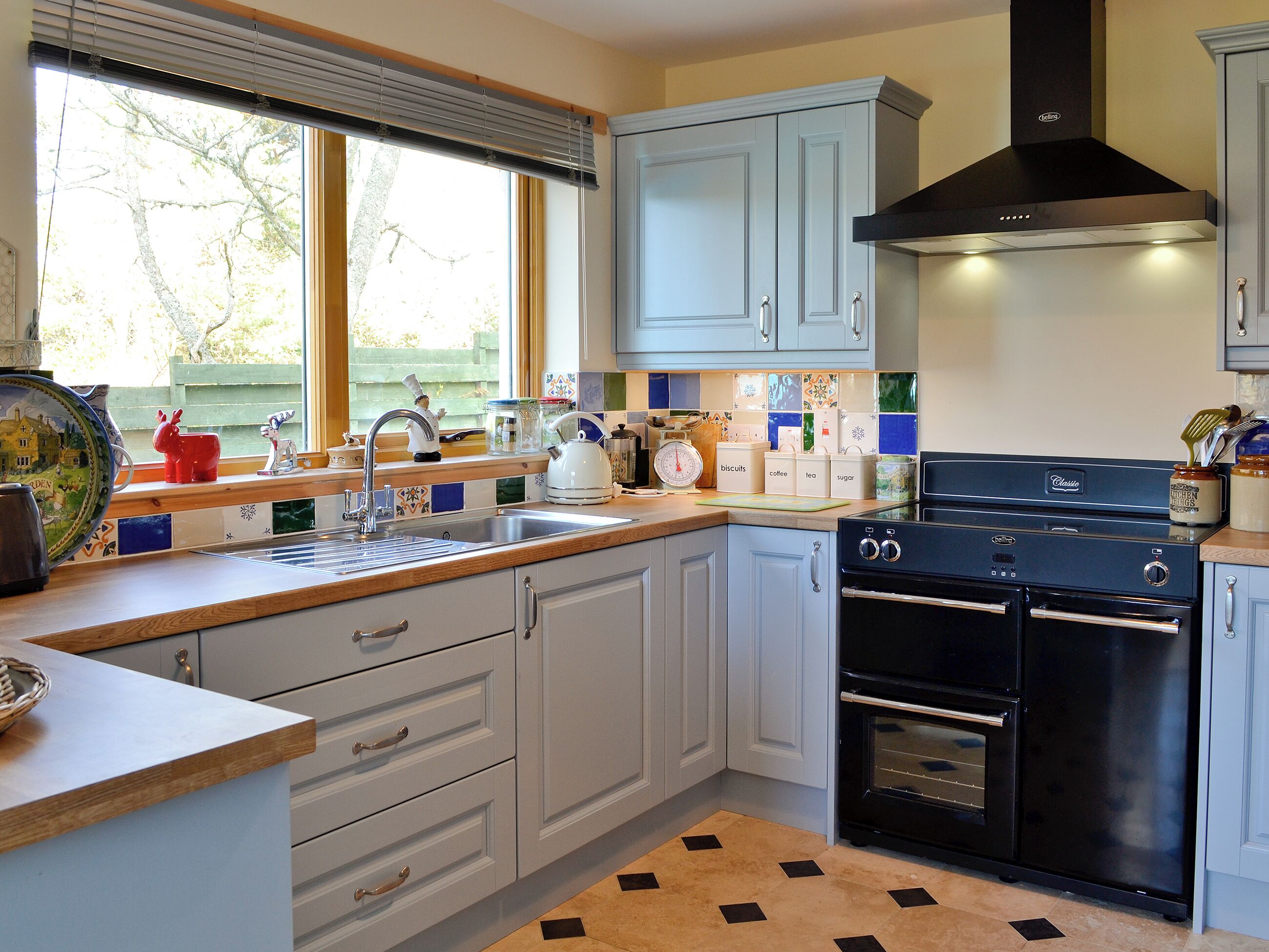 A kitchen with light blue cabinets, a black stove, and a window with blinds.