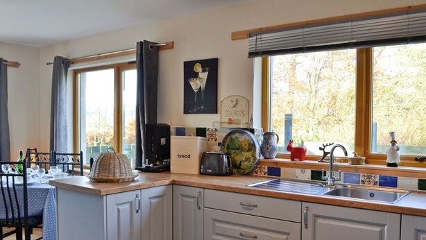 Una cucina moderna con mobili grigi, un piano di lavoro in legno, una macchina per il caffè e una finestra con vista sugli alberi.