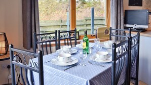 Una tavola da pranzo imbandita per quattro, con una tovaglia a pois blu, circondata da sedie con struttura in metallo nero. Sul tavolo, una bottiglia di liquore e dei bicchieri.