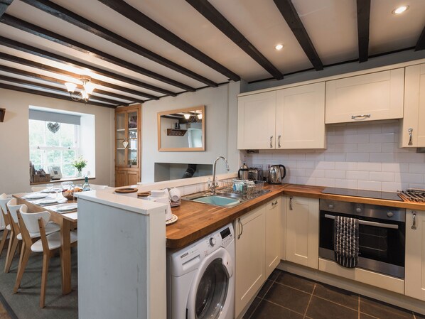 A compact kitchen with a built-in washing machine, a stove, and a sink. - 4 bedroom accommodation in Beddgelert (Beddgelert)