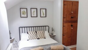 Une chambre à coucher comprenant un lit, une table de chevet, une armoire en bois et trois reproductions botaniques encadrées accrochées au mur.