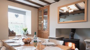 Une salle à manger avec une table en bois dressée pour quatre personnes, une cheminée et un grand miroir au-dessus du manteau de la cheminée.