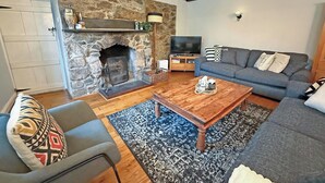 Un salon avec une cheminée en pierre, un canapé gris, une table basse en bois et un téléviseur.