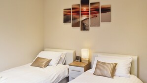 Camera d'albergo con due letti, un comodino con una lampada e un'opera d'arte a parete raffigurante un tramonto sulla spiaggia.