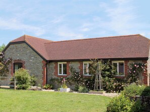 A stone house with a red-tiled roof, a brick chimney, and a garden with flowering plants.