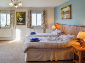 A double bed with a wooden headboard, two bedside lamps, and a painting above it.