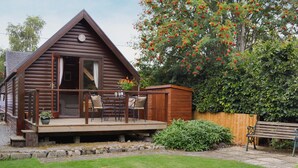 A wooden cabin with a deck, a patio table with chairs, and a small shed. - 2 bedroom accommodation in Blair Atholl near Pitlochry (Blair Atholl near Pitlochry)