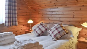 A wooden cabin room with a bed, two bedside lamps, plaid pillows, and a stack of towels. - 2 bedroom accommodation in Blair Atholl near Pitlochry (Blair Atholl near Pitlochry)