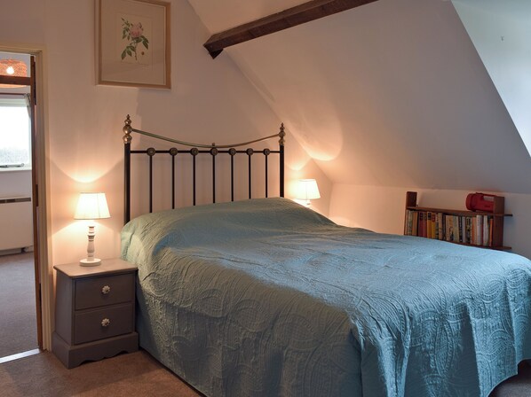 A bedroom with a bed, bedside lamps, a nightstand, a bookshelf, and a framed botanical illustration on the wall.