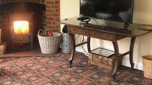 A room with a brick fireplace, a television on a wooden table, and a patterned rug. - 2 bedroom accommodation in Stanhoe, near King&rsquo;s Lynn (Stanhoe, near King&rsquo;s Lynn)