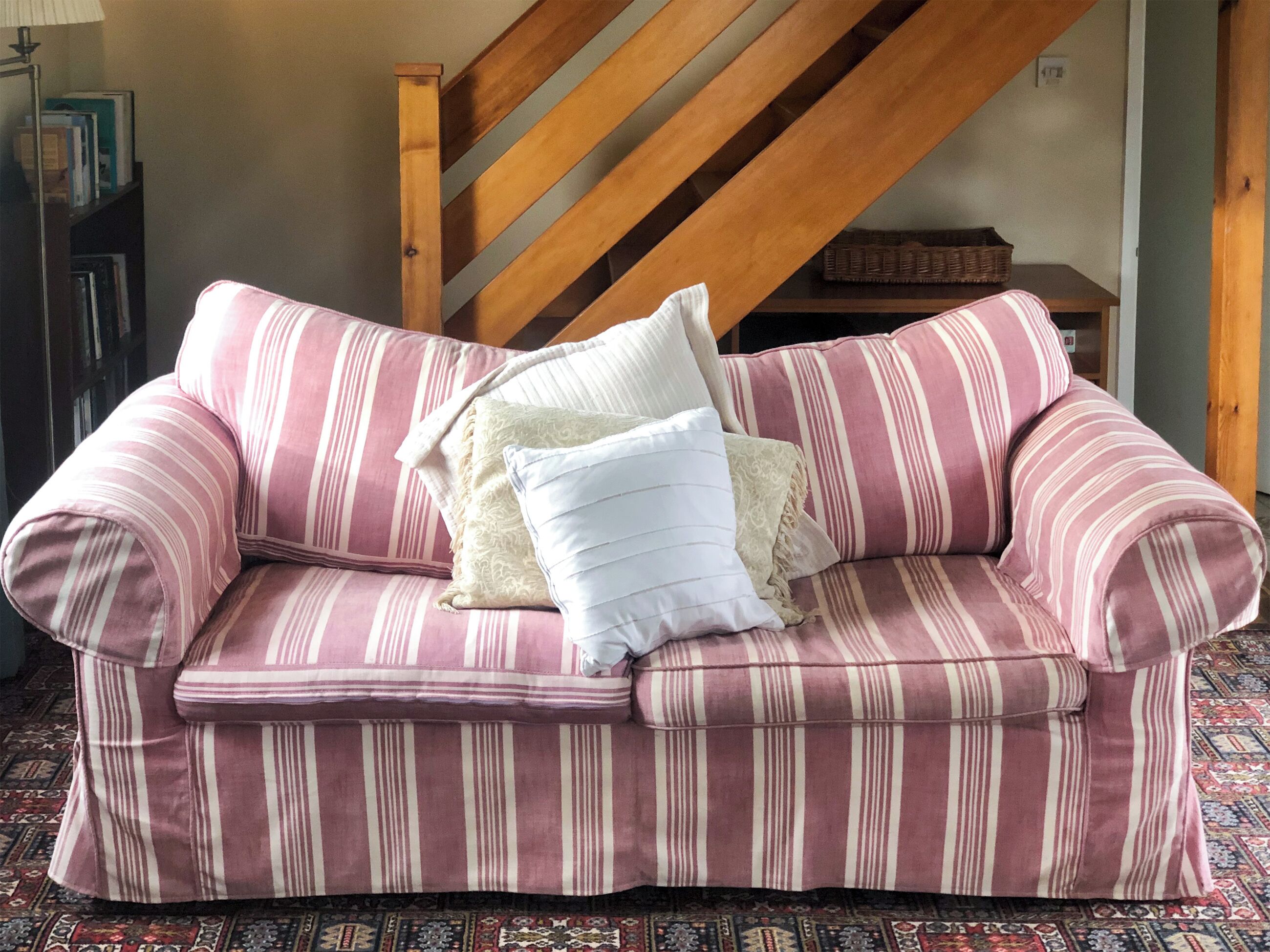 Ein gestreiftes rosa Sofa mit Kissen in einem Zimmer mit einer Holztreppe und einem gemusterten Teppich.