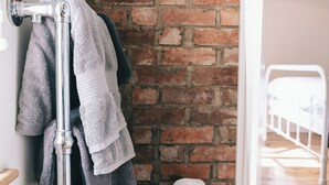 Une salle de bain avec un mur en briques, un porte-serviettes avec plusieurs serviettes et un panier de papier toilette.